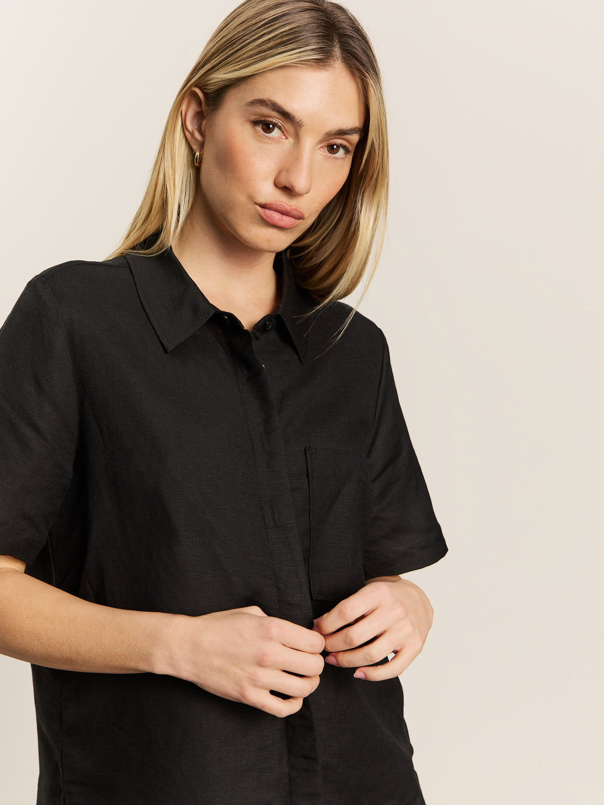 A person with long blonde hair wears the Sanctuary Clothing relaxed vacation shirt in black, standing against a plain light background and looking slightly to the side with a neutral expression.