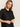 A person with long blonde hair wears the Sanctuary Clothing relaxed vacation shirt in black, standing against a plain light background and looking slightly to the side with a neutral expression.