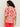 A person with curly hair wears the Sanctuary Clothing relaxed vacation shirt sunny riviera, featuring a bold red abstract sun and wave pattern on beige, paired with red pants. They face away from the camera against a plain background.