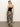 A woman with long blonde hair is wearing a Sanctuary Clothing "Meet Me at Sea" midi dress in black mirage. Walking on a smooth floor in black heels, she is set against a plain white wall.