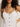 A person with curly hair is wearing the wilder linen dress bleached white by Sanctuary Clothing. The image highlights the upper body and part of the face against a neutral background.