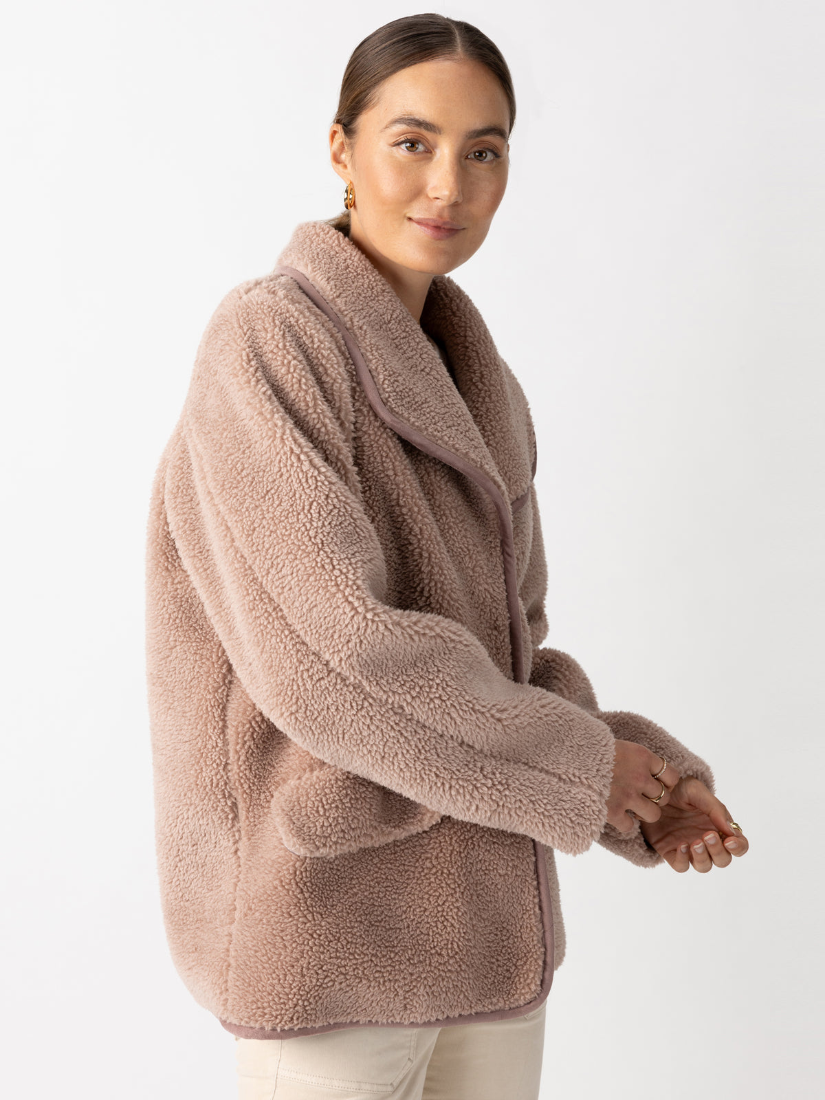 A person wearing a cozy Holly Sherpa Jacket Feather from Sanctuary Clothing poses against a plain background. They have their arms slightly crossed, with a subtle smile and hair neatly tied back. The jacket has a soft, textured appearance.