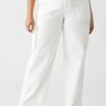 A person is wearing the Reissue Cargo White Inclusive Collection pants by Sanctuary Clothing. The high-waisted, wide-leg cargo pants with side pockets are paired with white sneakers. The person's upper outfit and head remain outside the frame, against a plain white background.