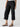 A person is wearing the Cali Cargo Pant Black by Sanctuary Clothing, featuring multiple pockets and rolled up to mid-calf length. They are also sporting black ankle-strap sandals, with a partially visible white top. The background is plain and light-colored.