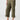 Person wearing Sanctuary Clothing's Cali Cargo Pant in Mossy Green, which features multiple pockets and rolled-up cuffs, paired with tan flat sandals. The person’s hand is resting in their pocket, and they are standing against a plain background. Only the lower half of the body is visible.