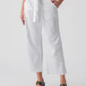 A person wearing the Reissue 90S Sash White pants by Sanctuary Clothing, which are white, wide-legged, cropped with a tied waist, and sandals with black straps and gold buckles. The pants feature large front pockets and seam details.