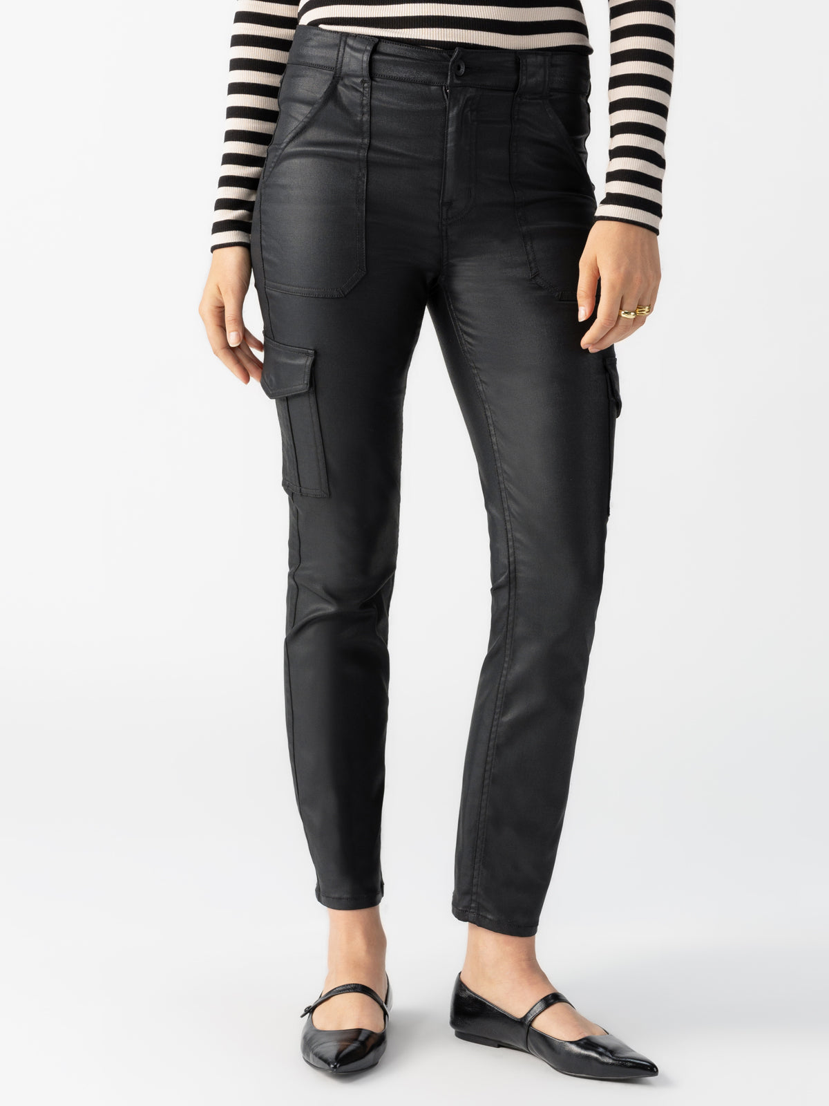 A person wearing the Sculpted Hayden Cargo Slick Black pants by Sanctuary Clothing, which are high-waisted with front and side pockets. They pair it with a black-and-white striped long-sleeve top and black flats.