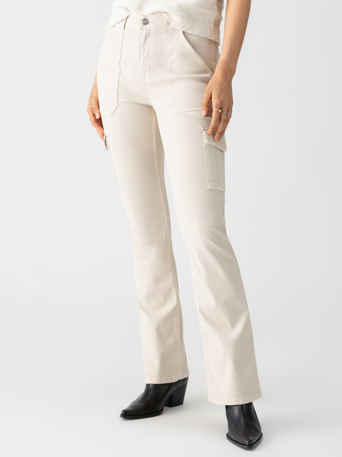 A person wearing off-white high-waisted cargo pants with front and side pockets, paired with the Sculpted Hayden Bootcut Toasted Almond boots from Sanctuary Clothing. The pants have a button and zip closure and are styled with a casual white top. The background is plain white.