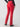 A person wearing the Velveteen Hayden Bootcut Pant in Mars Red from Sanctuary Clothing stands with their back to the camera. They have one arm by their side and the other bent at the elbow, with a black long-sleeved top and black heeled boots completing the outfit.