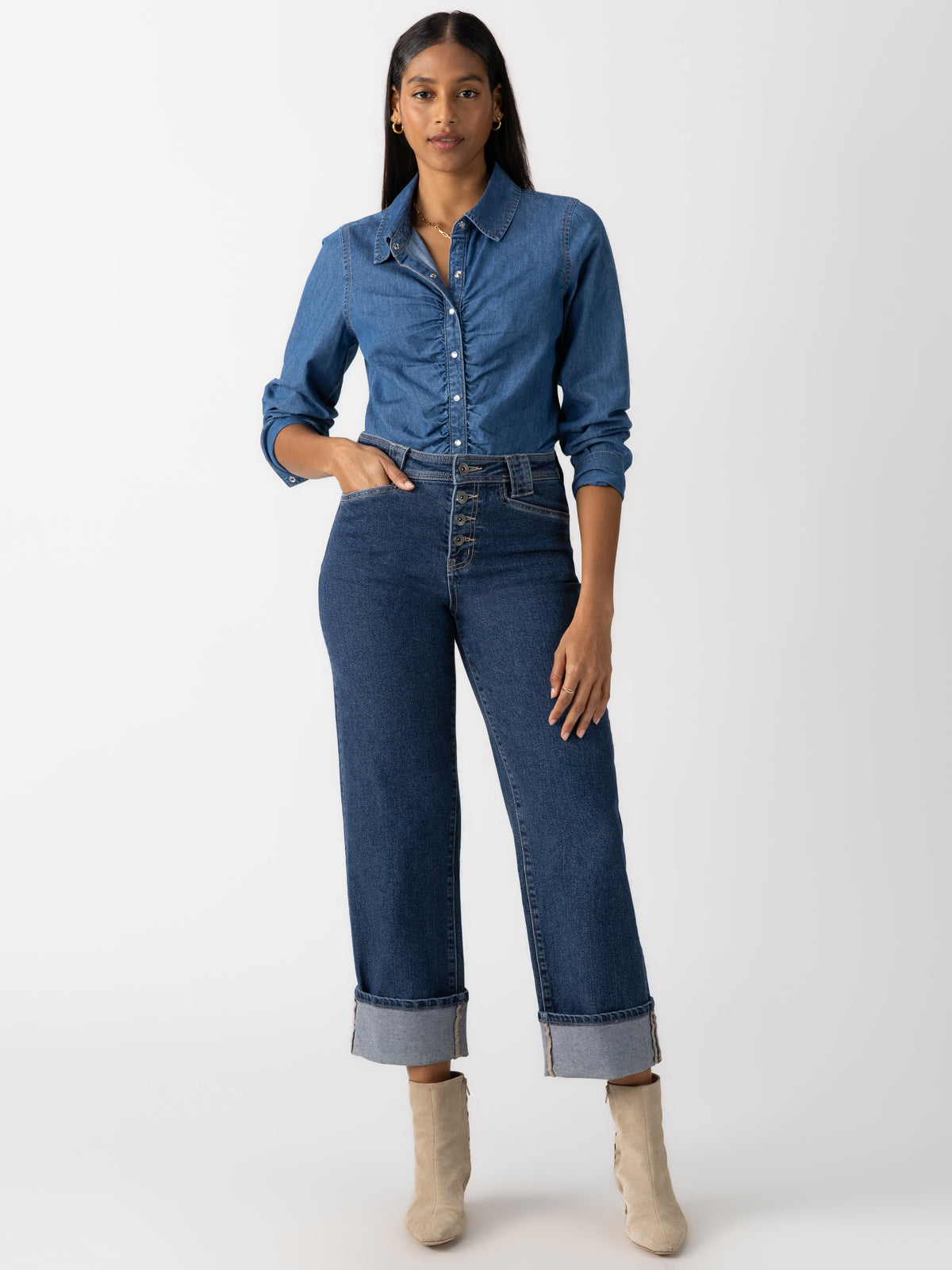 A person stands confidently in a full-length pose wearing a denim shirt paired with the Luna Cuffed Denim Pant Solstice from Sanctuary Clothing. They have long hair and are styling light-colored ankle boots against a plain white background.