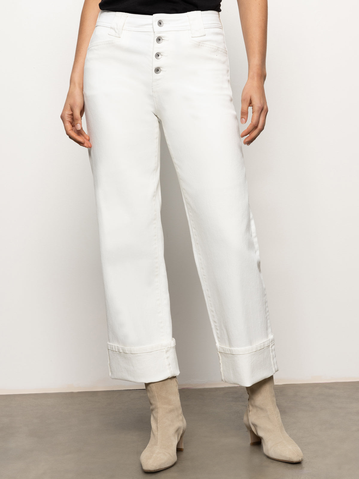 A person wearing the Luna Cuffed Denim Pant in bleached white by Sanctuary Clothing, paired with light-colored ankle boots. The background is a plain wall and floor, and the upper part of the person is not visible.