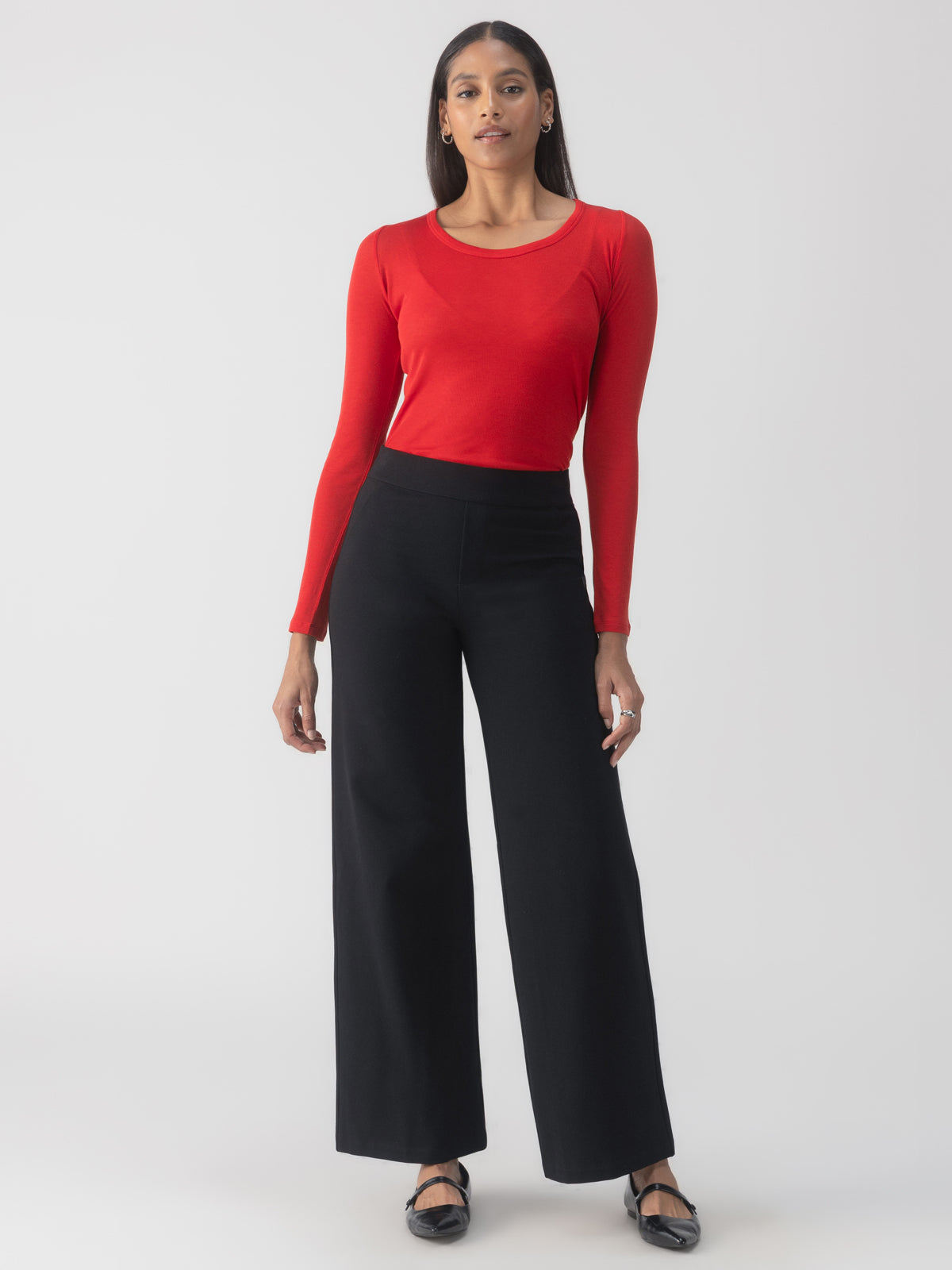 A person dressed in a red long-sleeve top and Sanctuary Clothing's Runway Ponte Trouser in Black stands against a plain background. They have long hair and are looking confidently at the camera.