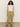 A person with long curly hair stands against a neutral background, wearing a white sleeveless top, Sanctuary Clothing's "Take Over" linen jogger pants in bamboo, and brown sandals.