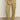 A person in the Sanctuary Clothing's "take over linen jogger" pants in olive green, featuring side pockets and elastic cuffs, is wearing brown sandals on a gray floor. Their hand rests casually on their thigh while donning a white shirt.