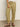 A person in the Sanctuary Clothing's "take over linen jogger" pants in olive green, featuring side pockets and elastic cuffs, is wearing brown sandals on a gray floor. Their hand rests casually on their thigh while donning a white shirt.