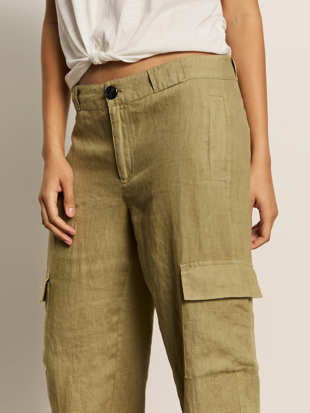 A person stands against a plain background, wearing Sanctuary Clothing's Take Over Linen Jogger Standard Rise Pants in bamboo with visible pockets, paired with a white tied crop top, showcasing only the lower half of their body.