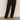 A person wearing the black take over linen jogger standard rise pant from Sanctuary Clothing and black sandals stands against a neutral background. Their hands hang casually by their sides. The pants feature multiple pockets, while the sandals boast a simple thong design.