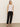 A woman stands casually against a plain backdrop, dressed in a white sleeveless top, Sanctuary Clothing's black "Take Over Linen Jogger Standard Rise Pant," and black sandals. Her long blonde hair cascades down as she maintains a neutral expression.