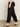 A person wearing Sanctuary Clothing's black "take over linen jogger standard rise pant" and black heeled sandals walks on a concrete floor, partially visible from the waist down, paired with a light-colored top.