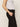 A person stands sideways, wearing Sanctuary Clothing's "take over linen jogger standard rise pant" in black with a pocket and a white sleeveless top. One hand rests in the pocket against a plain, light-colored background.