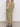 A person stands sideways in Sanctuary Clothing's area standard rise pant bamboo extended sizing, featuring olive green cargo style, paired with a black and white striped top and black sandals on a concrete floor against a plain light background.