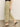 A person wears Sanctuary Clothing’s area standard rise pant bamboo in light olive, featuring wide legs and large front pockets, paired with a black top and black heeled sandals, standing on a smooth floor against a light background.