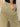 A person is seen from behind, wearing Sanctuary Clothing's area standard rise pant bamboo in light olive green, featuring visible stitching and large pockets, with one hand casually placed in the back pocket and paired with a black top.
