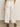 A person stands indoors, facing away, showing the lower back and legs in Sanctuary Clothing's area standard rise pant bleached white with patch pockets, paired with black sandals against a neutral background.