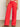 A person is casually standing, wearing Sanctuary Clothing's Highland Wide Leg Standard Rise Pant in cayenne with a patterned top. Their left hand rests on their side, and they wear open-toed sandals on a plain gray floor.