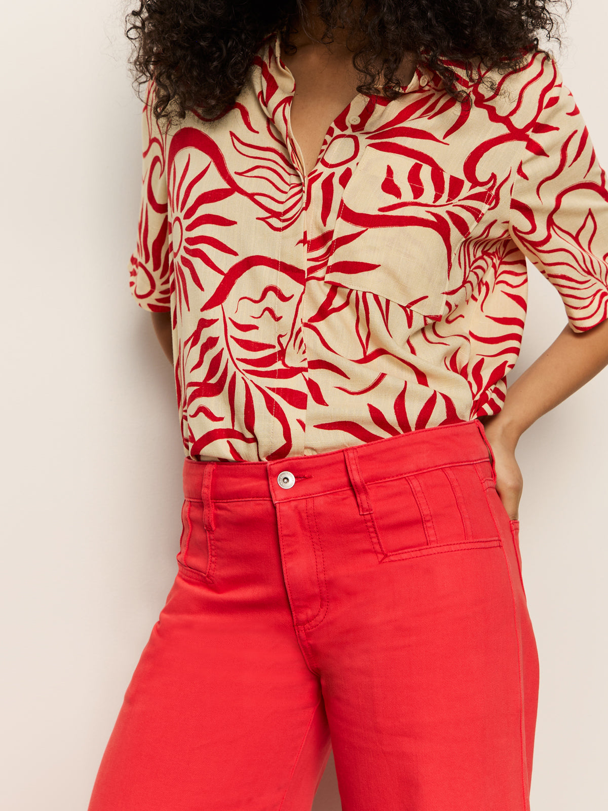 A person is wearing a beige and red abstract floral shirt with Sanctuary Clothing's highland wide leg standard rise pant in cayenne. They stand against a plain white background, with their face not visible.