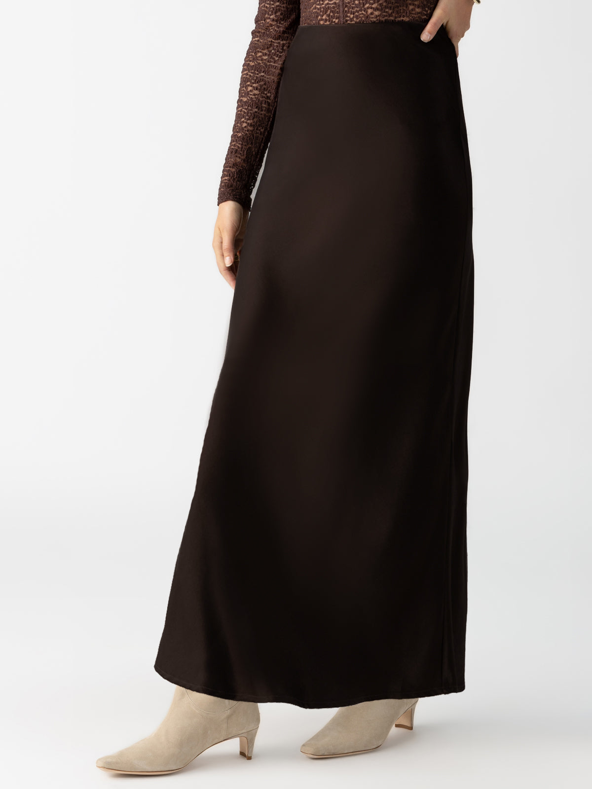 A person standing, wearing the Sanctuary Clothing Everyday Maxi Skirt in Coffee and beige ankle boots. They have on a brown patterned long-sleeve top. The background is plain white. The person's face is not visible in the image.