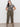 A person with long dark hair confidently poses against a plain background, wearing the Sanctuary Clothing "the perfect tee mirage extended sizing," paired with olive green pants and black sandals, casually placing their hands in their pockets.