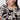 A person with dark hair wears gold hoop earrings and the Sanctuary Clothing "the perfect tee mirage extended sizing," a black and beige patterned shirt. They look slightly to the side with a neutral expression against a plain white background.