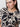 A person with dark hair wears gold hoop earrings and the Sanctuary Clothing "the perfect tee mirage extended sizing," a black and beige patterned shirt. They look slightly to the side with a neutral expression against a plain white background.