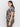 A person with long dark hair is wearing Sanctuary Clothing's "The Perfect Tee Mirage Extended Sizing," featuring a black and beige pattern, paired with olive green pants. They are standing sideways against a plain white background, looking ahead with a neutral expression.