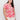 A woman models the Sanctuary Clothing "perfect tee sunny riviera extended sizing," featuring a bold red sun and wave pattern, paired with cream pants against a plain white backdrop. She has long, dark hair.