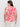 A woman, with her back to the camera, wears Sanctuary Clothing's "the perfect tee sunny riviera extended sizing," featuring a bold red floral pattern on cream. She pairs it with white pants against a plain white background.