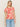 A person with long blonde hair is wearing Sanctuary Clothing's beige "the perfect tee sunny riviera" with a red abstract floral pattern and light blue jeans, standing against a plain background.