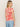 A woman with long hair, wearing the Sanctuary Clothing "The Perfect Tee Sunny Riviera," featuring a bold red floral pattern, paired with light blue jeans, stands against a plain background, looking to her right.