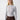 A woman with long blonde hair stands in front of a plain white background. She is wearing The Semi Sheer Long Sleeve Mock Sky from Sanctuary Clothing, paired with brown high-waisted pants. She has a neutral expression and is facing the camera.