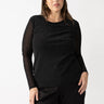 A woman with long brown hair is wearing the Sparkle Mesh Perfect Tee Black from Sanctuary Clothing's Plus Size Collection and dark pants. She is standing against a plain white background with her left hand resting on her hip, displaying a calm expression.