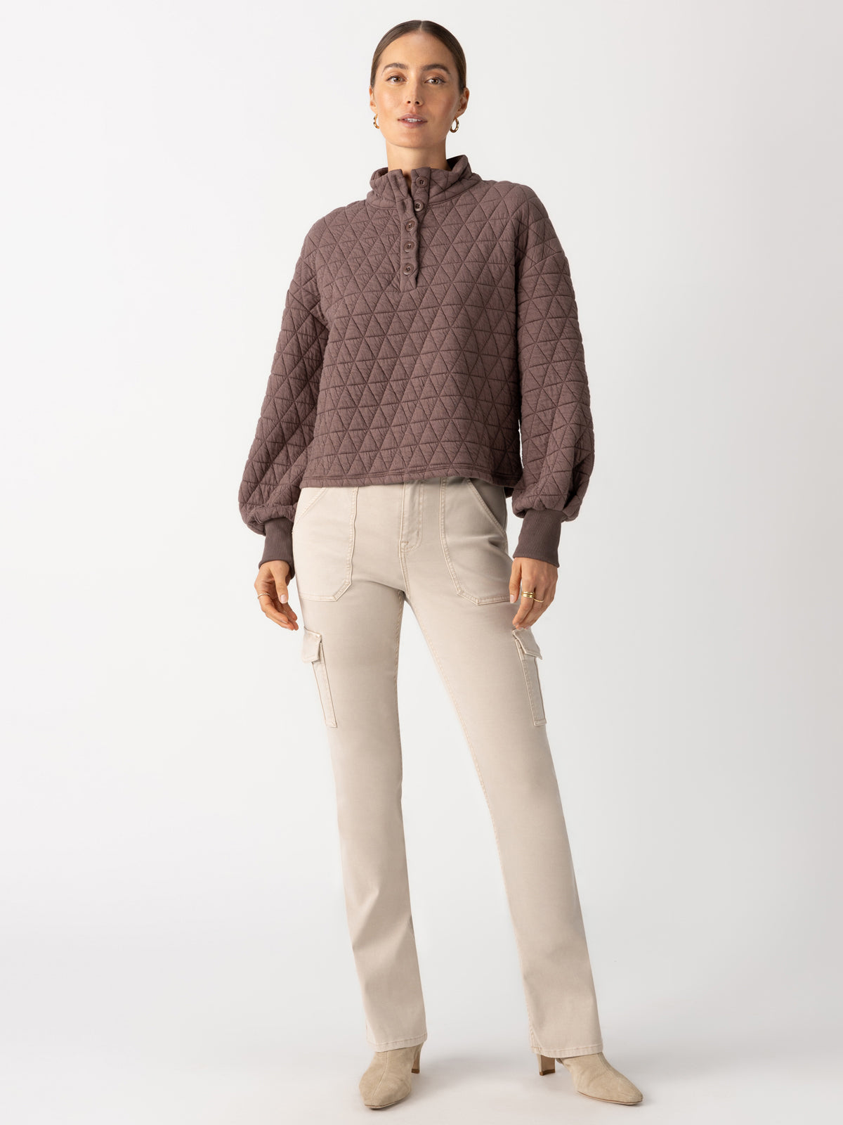 A person stands against a plain background, wearing the Quilted Button Up Popover Top in Cocoa by Sanctuary Clothing, along with beige cargo pants. They have short hair and are wearing beige shoes. Their hands are relaxed by their sides.