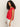Woman with long curly hair models the Sanctuary Clothing knotted muscle tee in cayenne, styled sleeveless and paired with white pants, standing sideways and looking at the camera against a light background.
