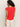 A woman with curly hair stands with her back to the camera, wearing the Sanctuary Clothing knotted muscle tee in cayenne and white pants against a plain light background.