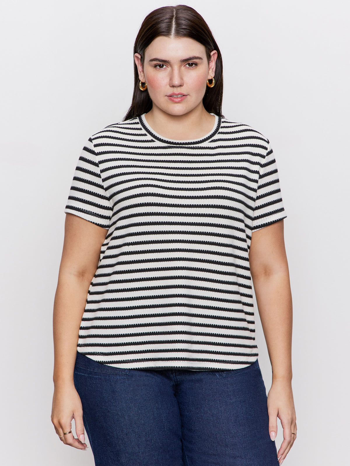 A person with long dark hair wears the perfect textured tee macrame black stripe from Sanctuary Clothing, paired with blue jeans. They're standing against a plain white background, sporting hoop earrings and a neutral expression.