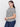 Wearing the Sanctuary Clothing "perfect textured tee macrame black stripe extended sizing" and blue jeans, a person with long dark hair stands sideways, smiling slightly at the camera. Simple jewelry complements their look against a plain, light-colored background.