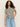 A person with long curly hair, wearing Sanctuary Clothing's "perfect textured tee macrame black stripe" and light blue jeans, stands against a plain background with a relaxed posture and one hand on their hip.