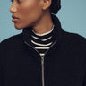 A person with their hair pulled back in a bun looks to the side against a blue backdrop, wearing the Sanctuary Clothing black alpine sherpa half zip popover over a black and white striped turtleneck.