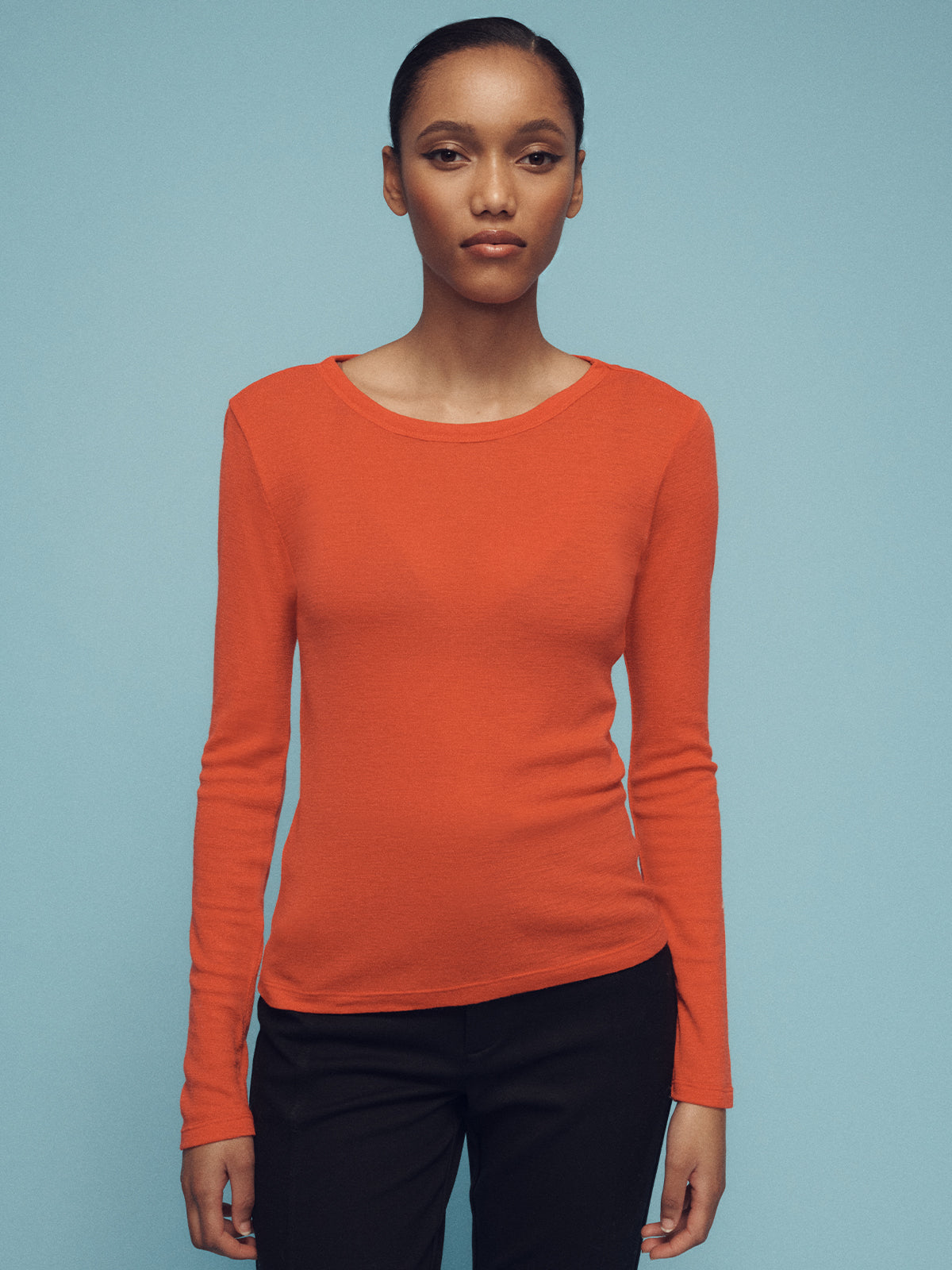 A person wearing Sanctuary Clothing's long sleeve wool perfect tee in orange and black pants stands against a light blue background.