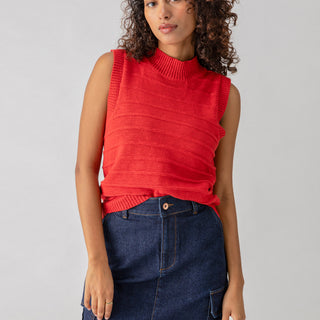 A person with curly hair is wearing the Sanctuary Clothing Life Is Easy Shell Cherry Red and a high-waisted, dark blue denim skirt. They are standing against a plain gray background, looking confidently at the camera with a relaxed expression.